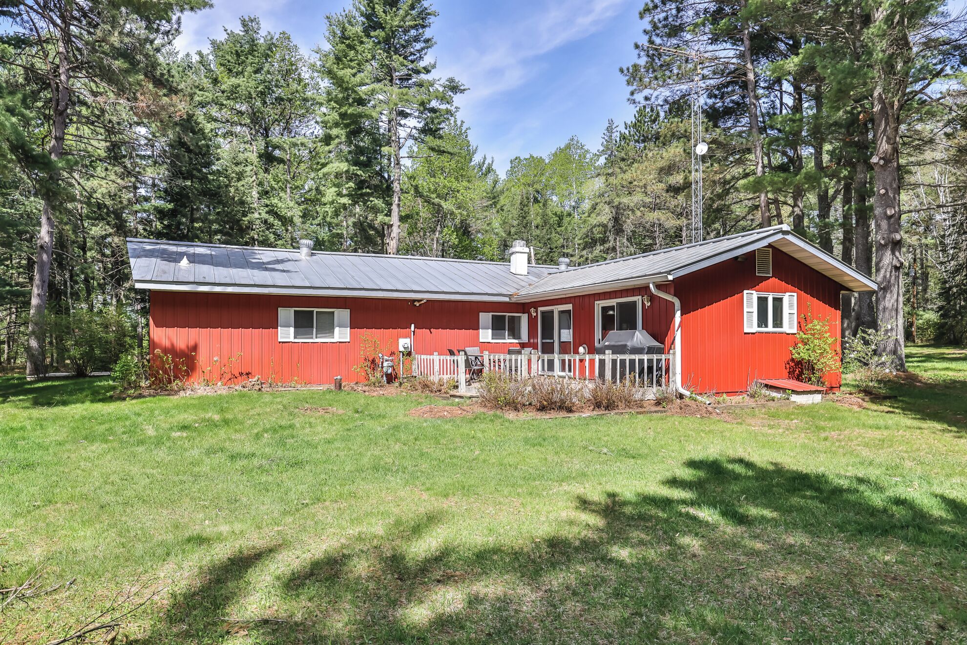 A red cabin with a porch, surrounded by a grassy yard and tall trees.