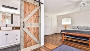 A bedroom with a wooden floor, a bed, a nightstand, a dresser, and a sliding barn door. - Stepaway Vacation Rentals- Happy Hours Pet Friendly (Eagle River)