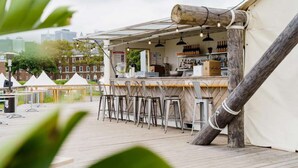 Ein Außenbereich mit Bar, einer Holzterrasse, Barhocker und einer rustikalen Holzhütte.