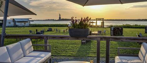 A deck with outdoor seating, a view of the Statue of Liberty, and a sunset over the water.