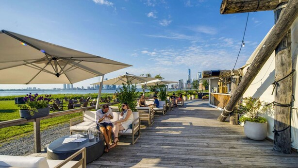 Eine Holzterrasse mit Gartenmöbeln, Sonnenschirmen und Blumentöpfen.