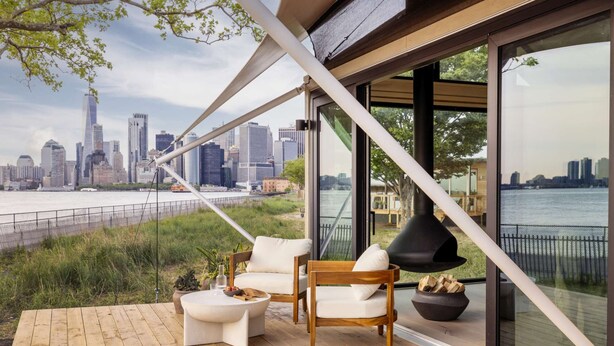 A modern outdoor seating area with a city view, wooden deck, and a fireplace. - Luxurious Glamping | Panoramic Views & Dining (New York)