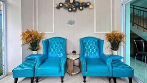 Ein Zimmer mit zwei blauen Sesseln, die einander gegenüberstehen, einem kleinen runden Tisch und einer Wanddekoration.