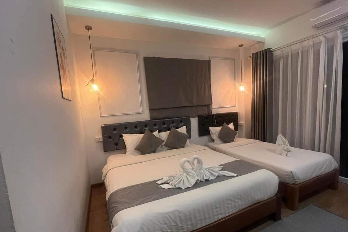 A hotel room with two beds, a large flat-screen TV, a ceiling light, and a window with curtains.