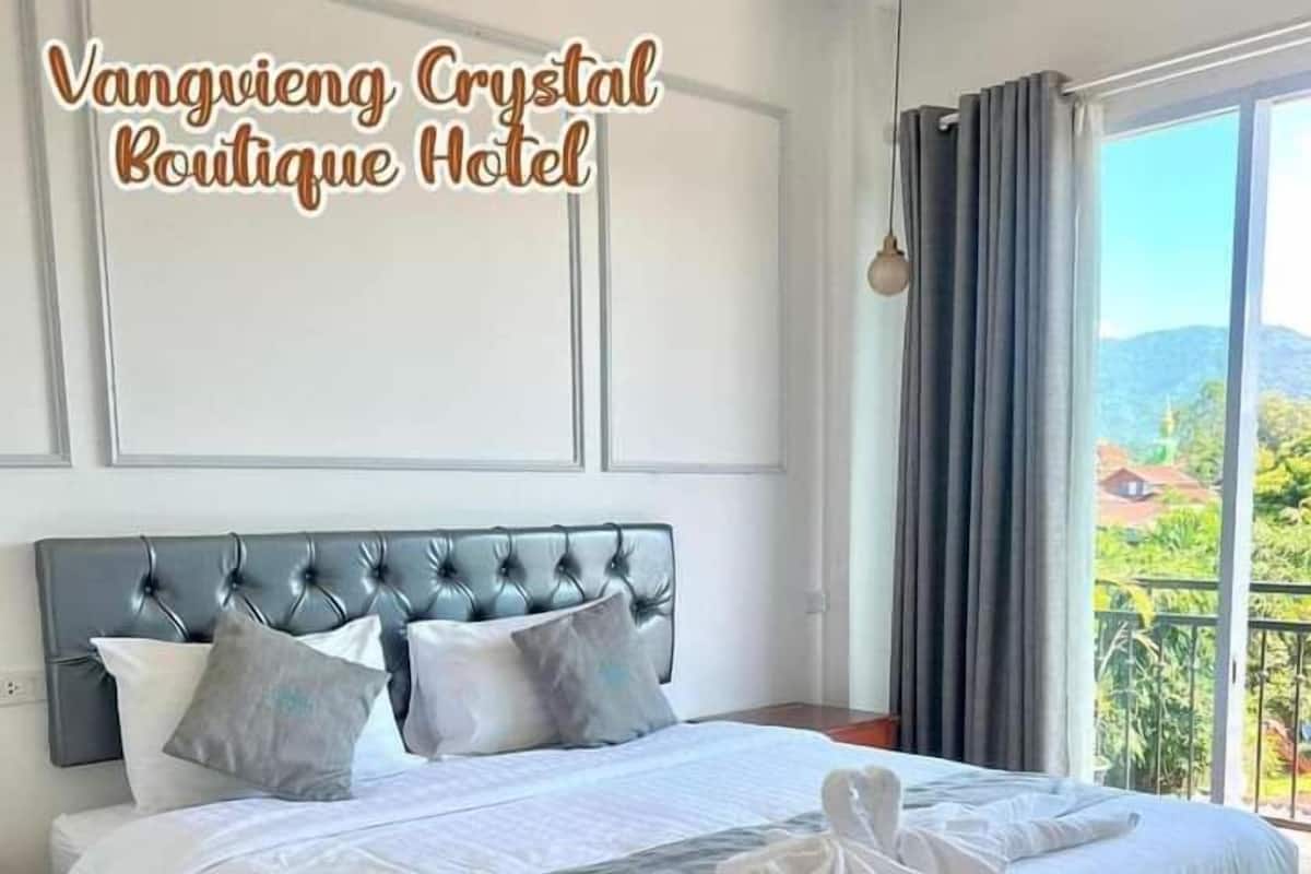 A hotel room with a large bed, a headboard, and a view of greenery outside.