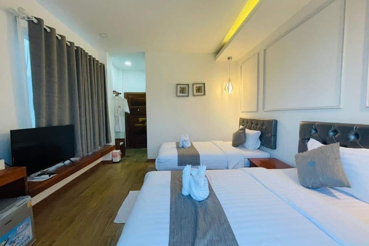 A hotel room with two beds, a flat-screen TV, wooden flooring, and a hallway leading to a bathroom.