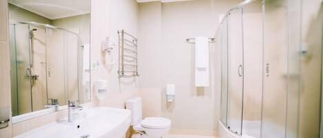 A modern bathroom with a large white bathtub, a toilet, and a glass-enclosed shower.