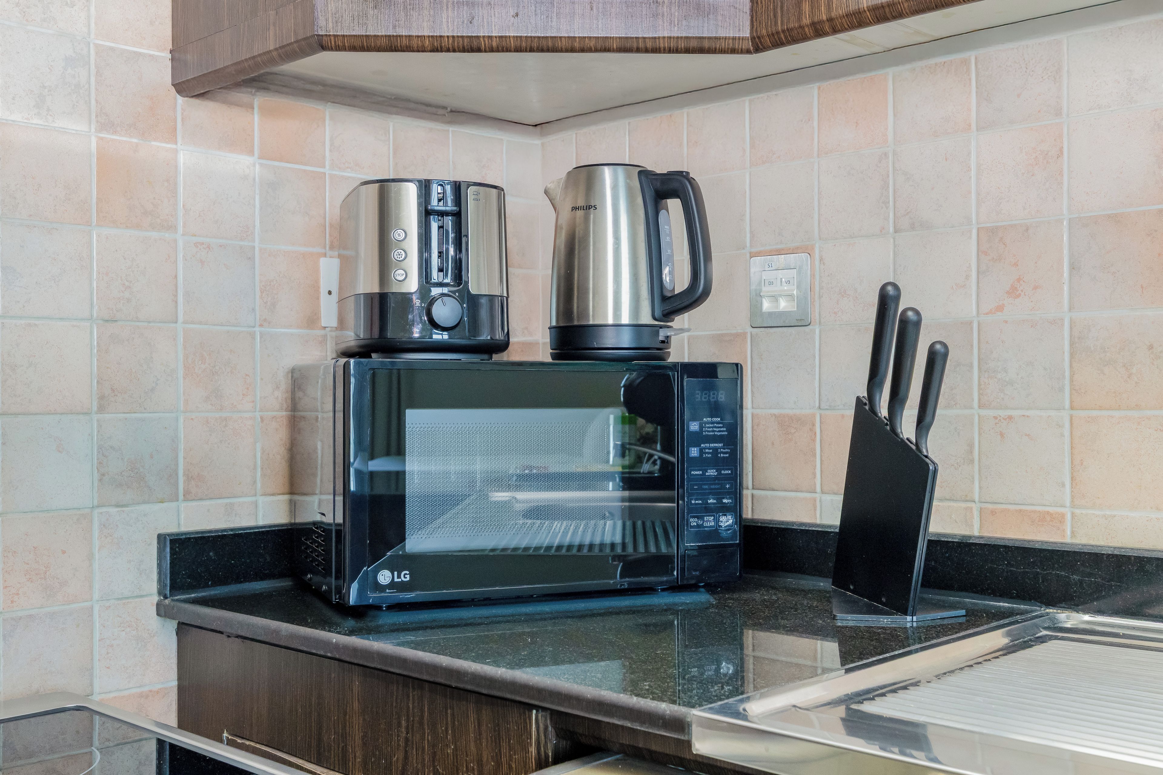 Una cocina con microondas, cafetera y hervidor sobre la encimera.