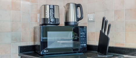 A kitchen with a microwave, a coffee maker, and a kettle on the countertop.
