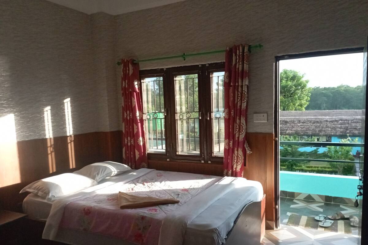 A bedroom with a bed, a window with curtains, and a view of a pool and greenery outside.