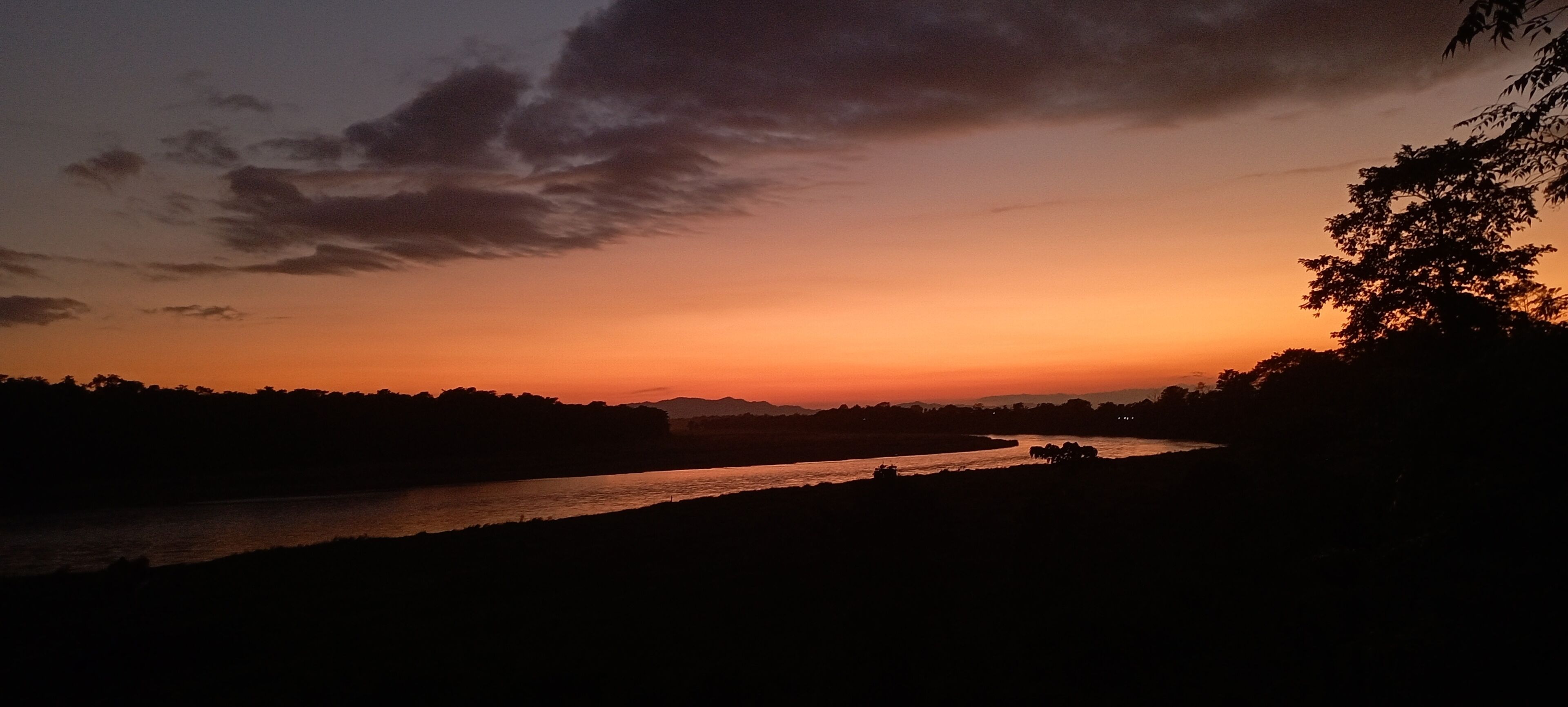 Un río al atardecer con el silueta de árboles y colinas al fondo.