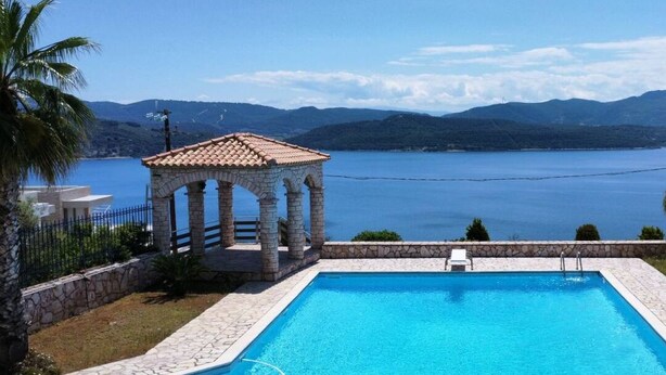 Ein Schwimmbad mit einer Steinterrasse, einem Pavillon und Blick auf einen See und Berge.