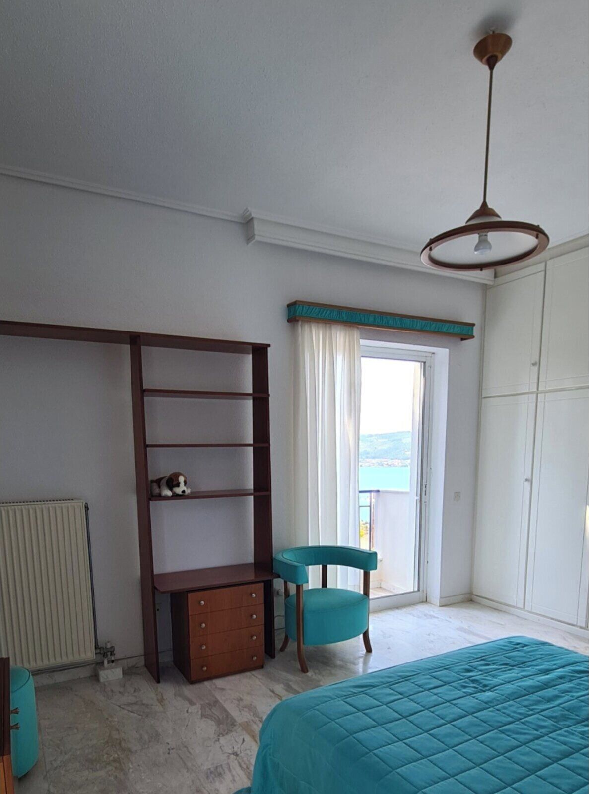 Une chambre à coucher avec un lit, un bureau, une chaise, un radiateur et une fenêtre avec des rideaux.