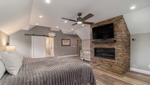 Ein Schlafzimmer mit Bett, Deckenventilator, Kamin und einem an einer Steinwand montierten Fernseher.