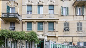 Un edificio de varios pisos con balcones, contraventanas verdes y una entrada con portón.