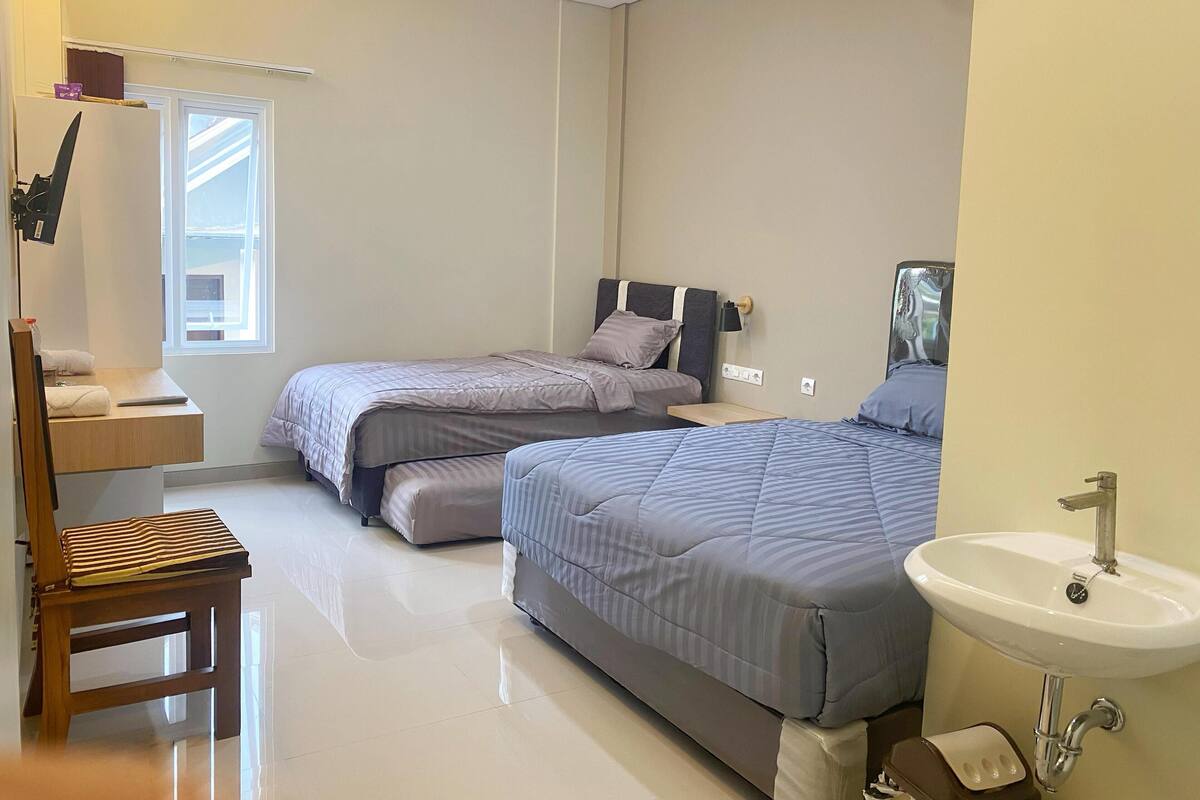 Un dormitorio con dos camas, una silla de madera, una mesita de noche, una ventana y un baño con lavabo.