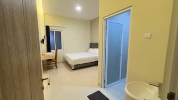 Un dormitorio con cama, escritorio, silla, puerta y baño con bañera.