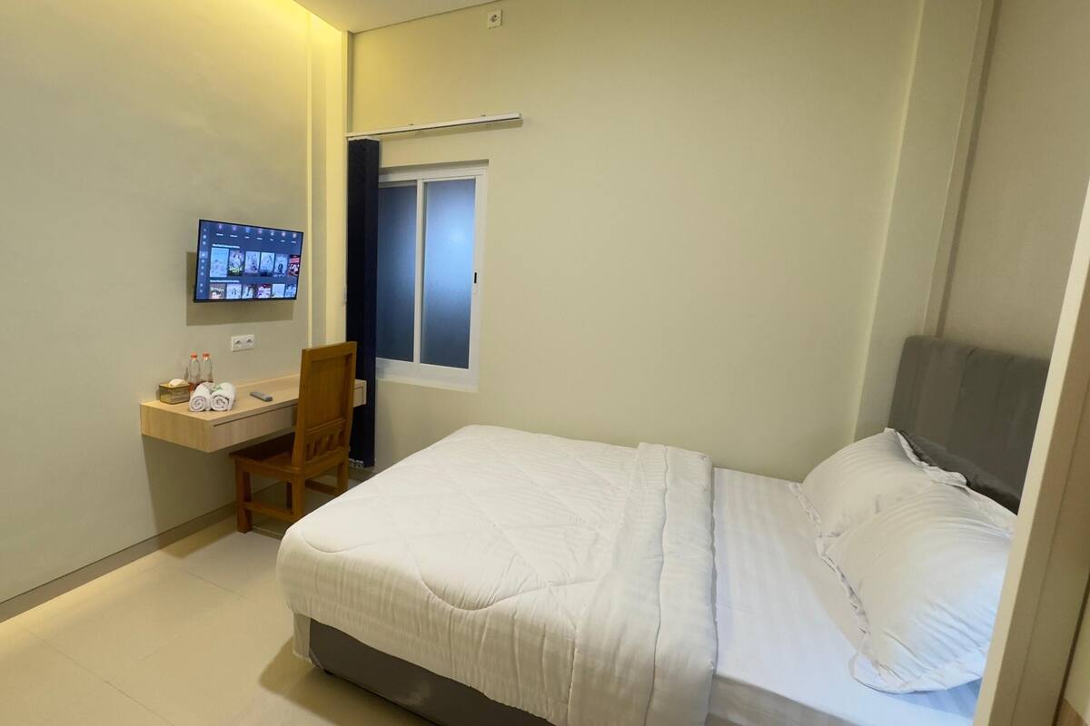 Un dormitorio pequeño y ordenado con una cama, un escritorio y un televisor montado en la pared.