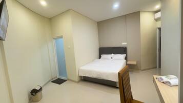 A bedroom with a bed, a bedside table, a small shelf, a door, and a trash bin.