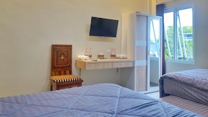 Ein Hotelzimmer mit zwei Betten, einem an der Wand befestigten Fernseher, einem kleinen Tisch mit Pflegeprodukten und einem Fenster mit Blick auf Grünflächen.