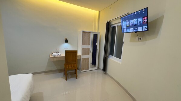 A hotel room with a desk, chair, and a TV mounted on the wall displaying movie options. - Nganjuk Family Guest House (Nganjuk)