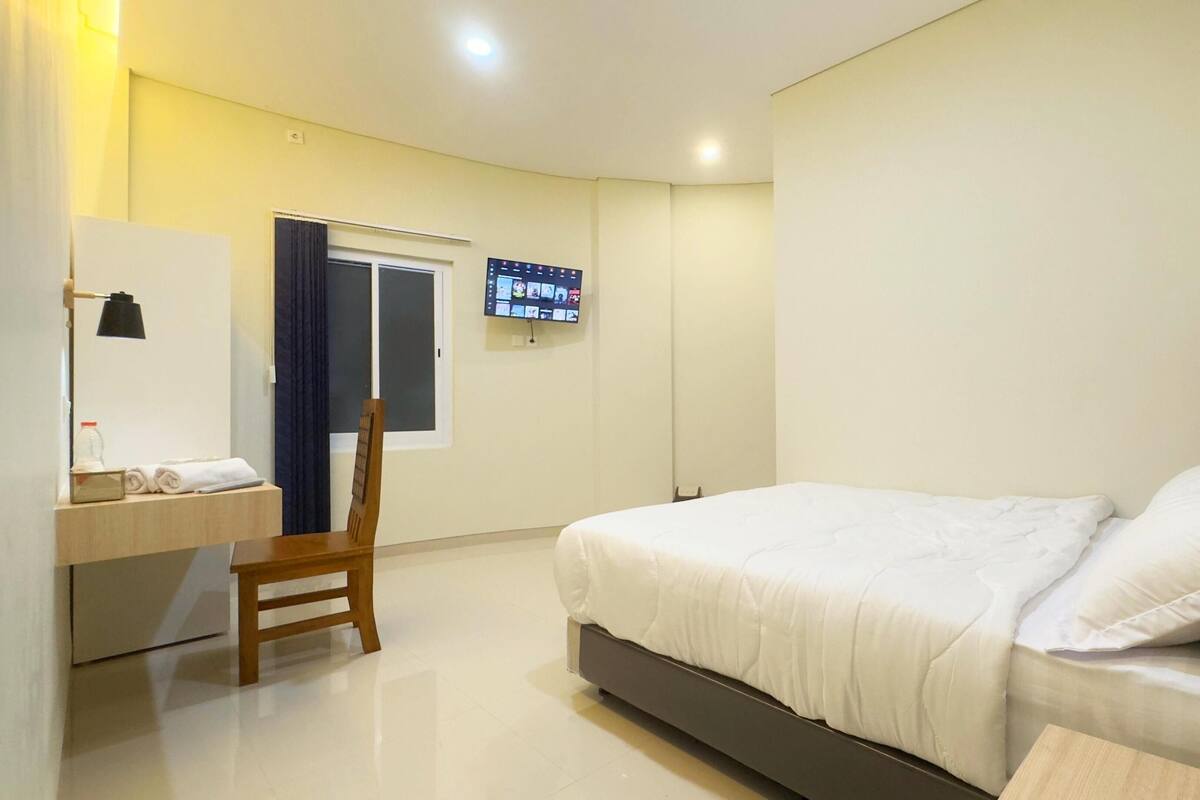 Una habitación de hotel con una cama, un escritorio con una silla, un televisor montado en la pared y una puerta.