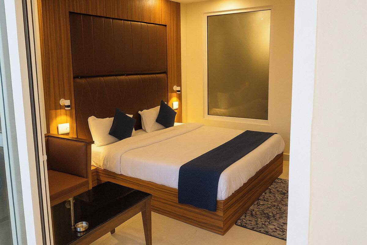 Cama bem arrumada com cabeceira de madeira, duas luminárias de cabeceira e uma mesinha com abajur.