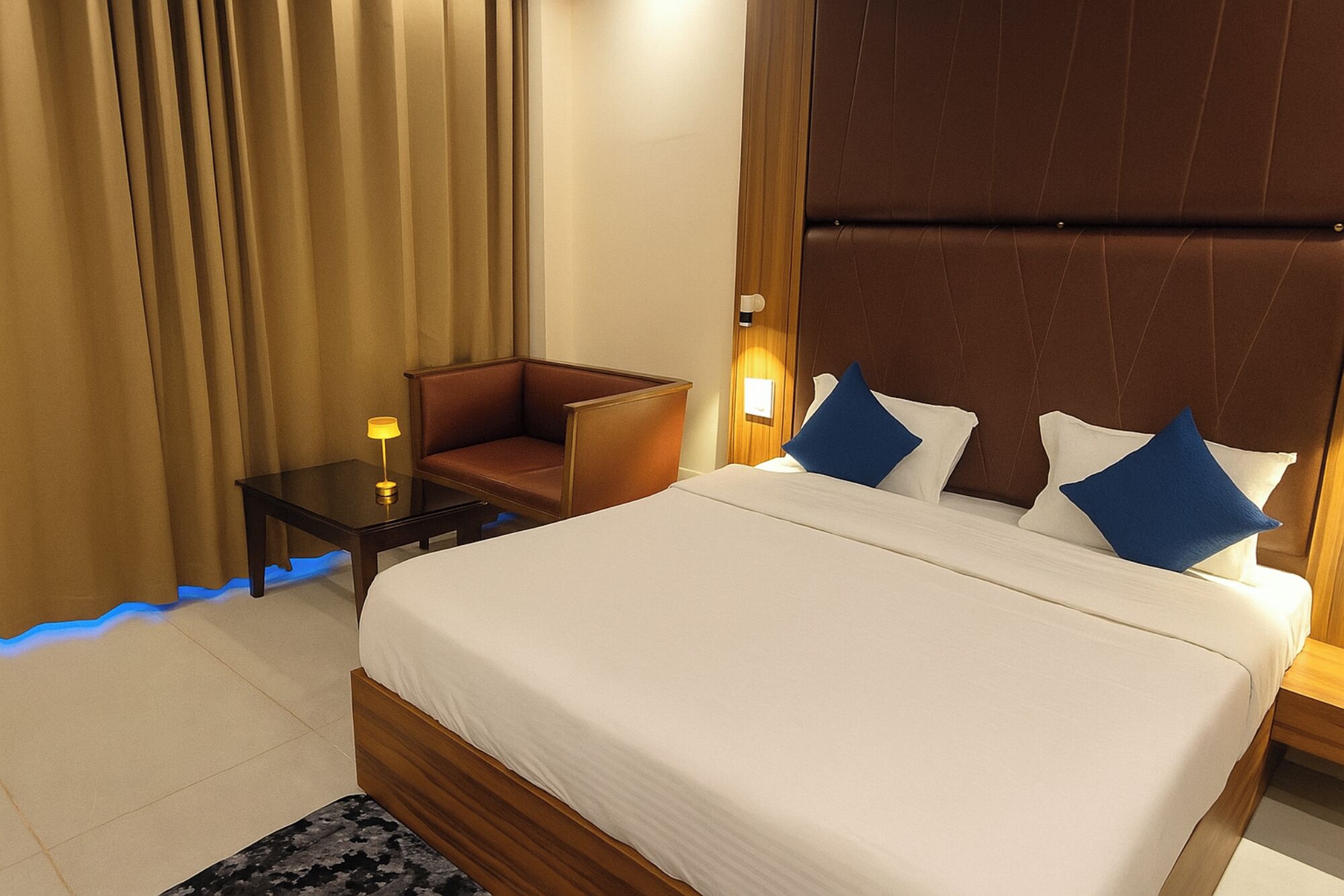 A hotel room with a large bed, a small table with a lamp, a chair, and a nightstand.