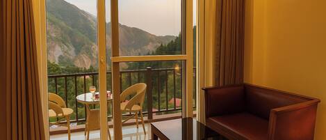 A balcony with a view of mountains, a glass table, wicker chairs, and a leather sofa.