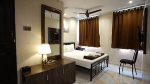 Ein Hotelzimmer mit einem Bett, einem Schreibtisch mit Lampe, einem Sessel und Vorhängen sowie einem Deckenventilator.