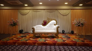Eine Bühne mit einem weißen, verzierten Sofa, Vorhängen und Blumenarrangements.