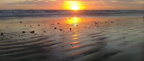 A beach at sunset with the sun low on the horizon, reflecting on the wet sand.