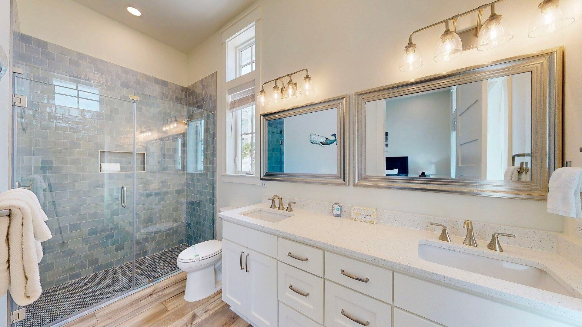A modern bathroom with a glass shower enclosure, a large mirror, and a white vanity with multiple sinks.