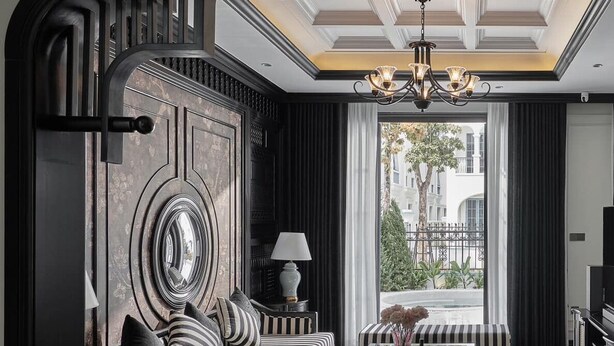 A modern living room with a sofa, armchairs, and a coffee table. A large mirror and a chandelier are visible.