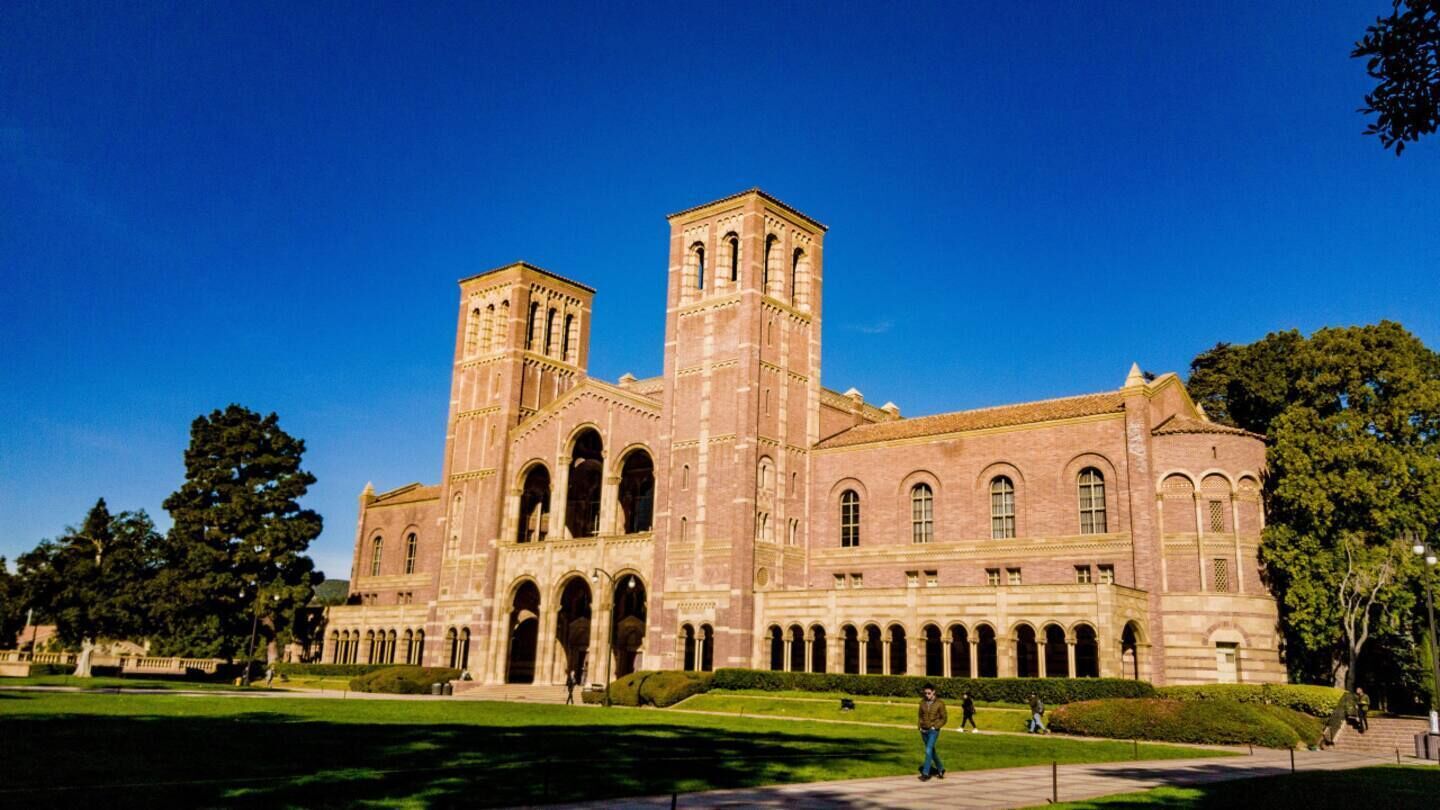A large, historic building with multiple arches and towers, surrounded by a well-maintained lawn and trees.