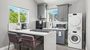 A compact kitchen with a central island, bar stools, a built-in washing machine, and a microwave.