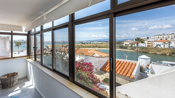Un balcón con ventanas amplias que dan a un río y un paisaje urbano.