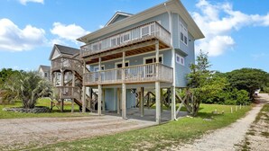 A two-story beachfront house with a wooden deck and multiple balconies.