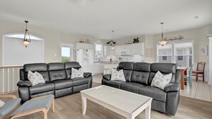 A modern living room with two black leather sofas, a white coffee table, and a dining area with a wooden table and chairs.
