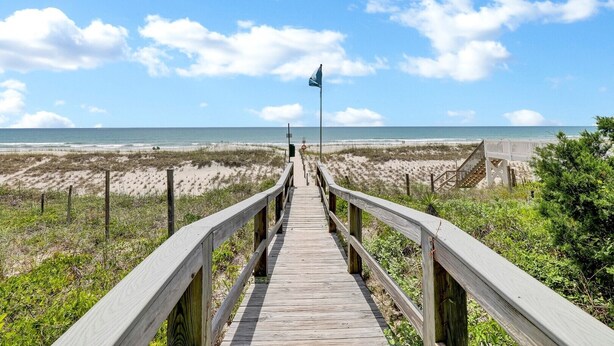 A wooden boardwalk leading to a beach with a flag at the end.