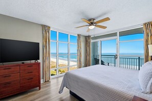 A hotel room with a large bed, a TV on a wooden dresser, and a balcony with a view of the beach. - 🌴Ocean View | Indoor Heated Water Park + Lazy River | Dunes Village Resort 937 (Myrtle Beach)