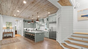 A modern kitchen with a central island, stainless steel appliances, and a wooden staircase. - Welcome to Azalea Abbey! Private Pool, Golf Cart, Walk to Beach, Seaside (Santa Rosa Beach)