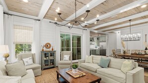 A spacious living room with a wooden ceiling, white walls, and a large window. There are two sofas, a coffee table, and a dining table with chairs. - Welcome to Azalea Abbey! Private Pool, Golf Cart, Walk to Beach, Seaside (Santa Rosa Beach)
