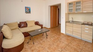 Una sala de estar con un sofá y una mesa de centro, una cocina con gabinetes de madera y una puerta que da a otra habitación.