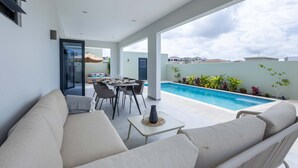 Un espacio exterior moderno con piscina, comedor y sofá.