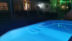 A swimming pool at night with steps leading into it, surrounded by a patio area with outdoor seating and ambient lighting. - Boho Sisi Haven- Poolside Oasis Garden Retreat (Agios Nikolaos)