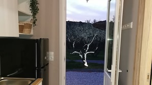 A narrow kitchen with a black refrigerator, a wooden countertop, and a sink. A door leads to a gravel area with a tree. - Boho Sisi Haven- Poolside Oasis Garden Retreat (Agios Nikolaos)