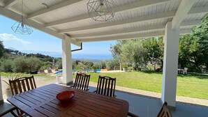 A covered patio with a wooden table and chairs, overlooking a well-maintained lawn and distant hills. - Tenute Lomasi - near Cefalù with swimming pool (Lascari)