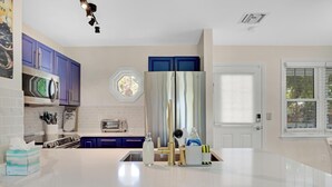 A modern kitchen with white countertops, a stainless steel refrigerator, and blue cabinets.