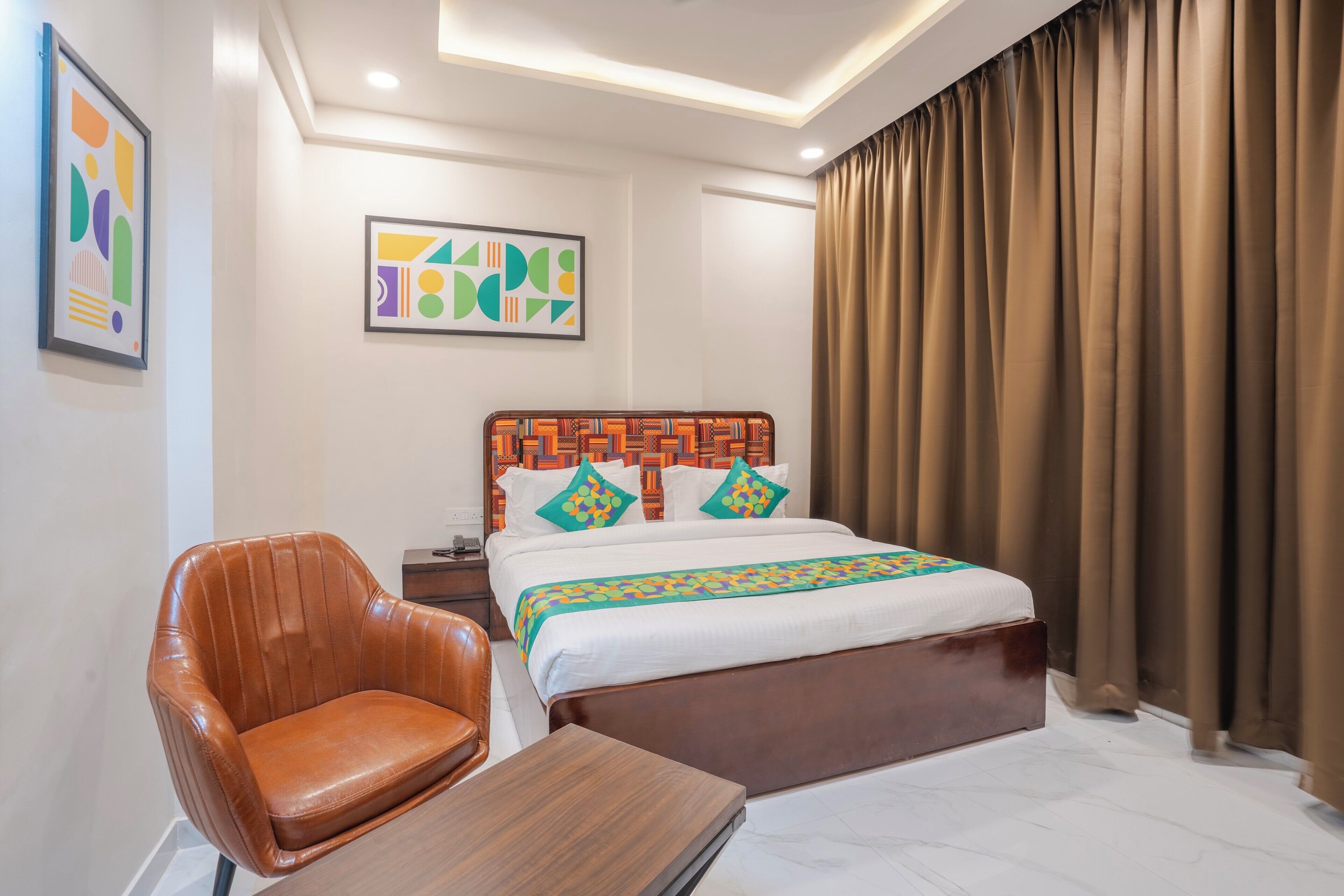 Une chambre d’hôtel avec un lit, une chaise, une table de chevet et des œuvres d’art accrochées aux murs.